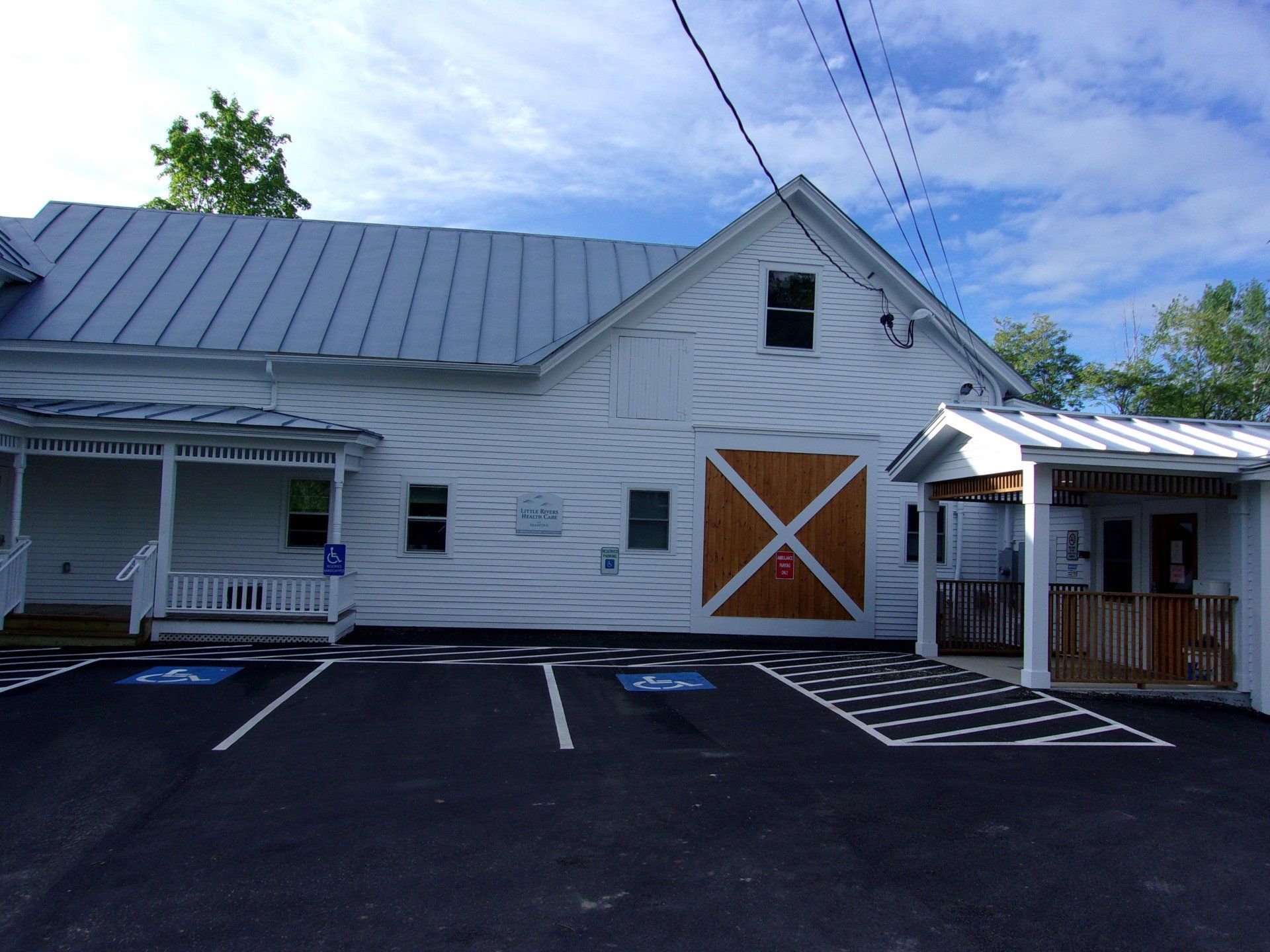White barn with metal roof, orange sliding doors, and empty parking lot under a blue sky