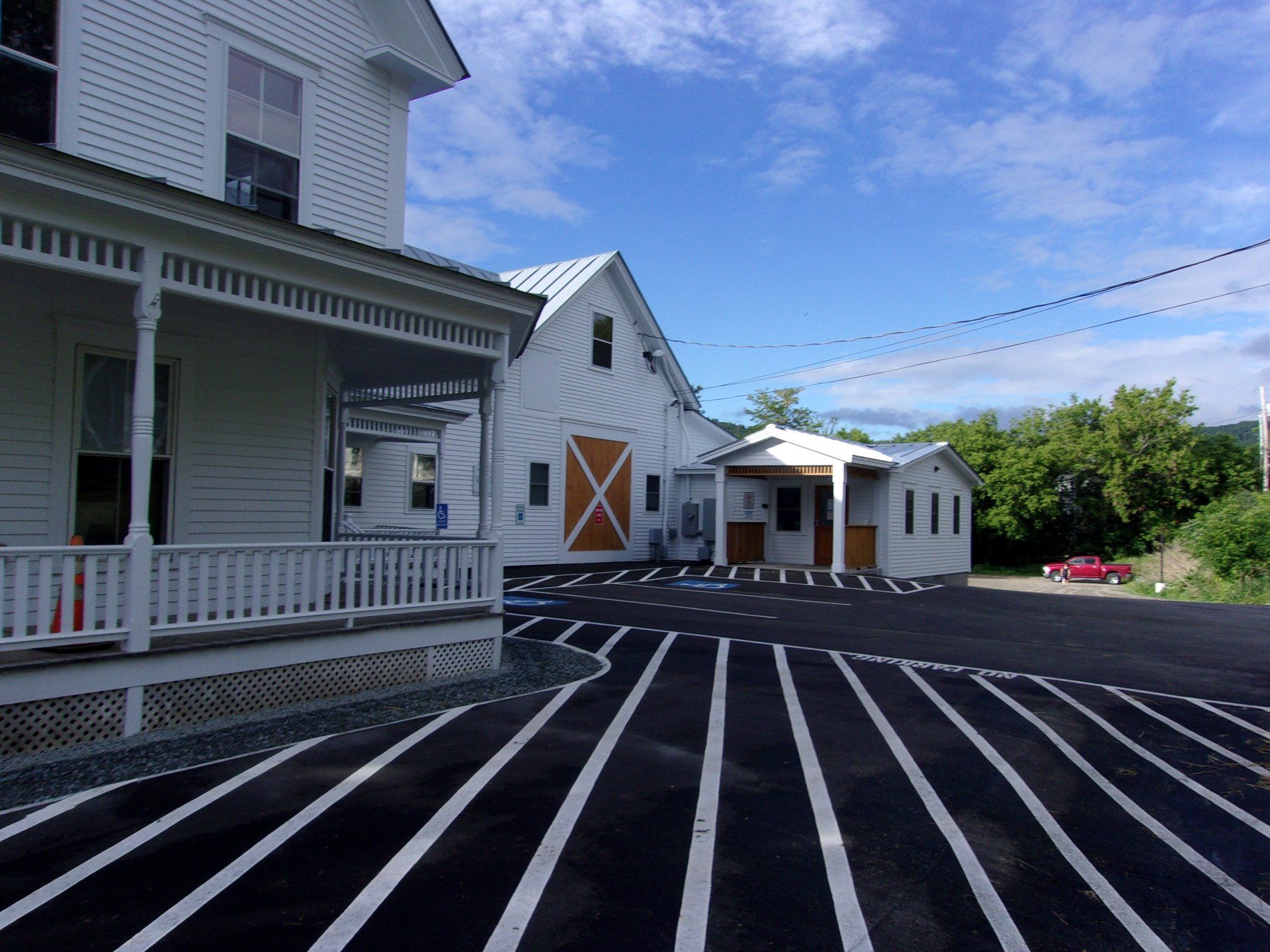 White farmhouse and barn with striped asphalt parking lot under a blue sky