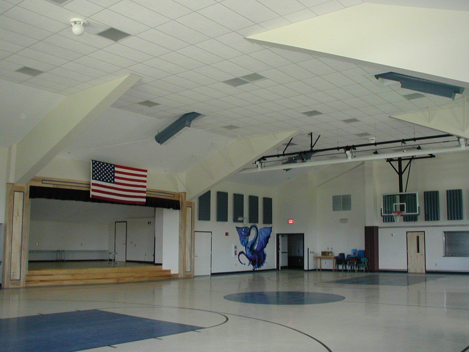 Empty school gymnasium with stage, American flag, and blue painted floor circles