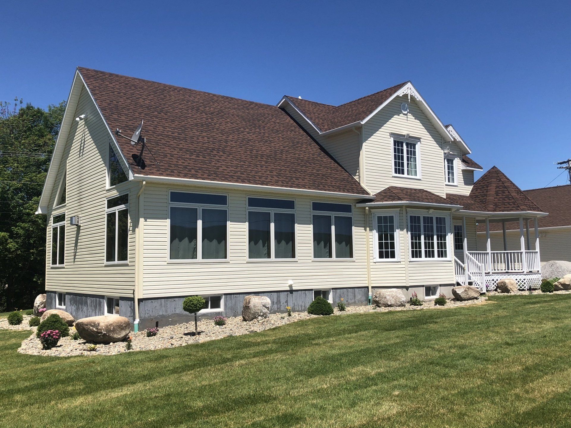 Large beige house with brown roof and white trim on a sunny lawn