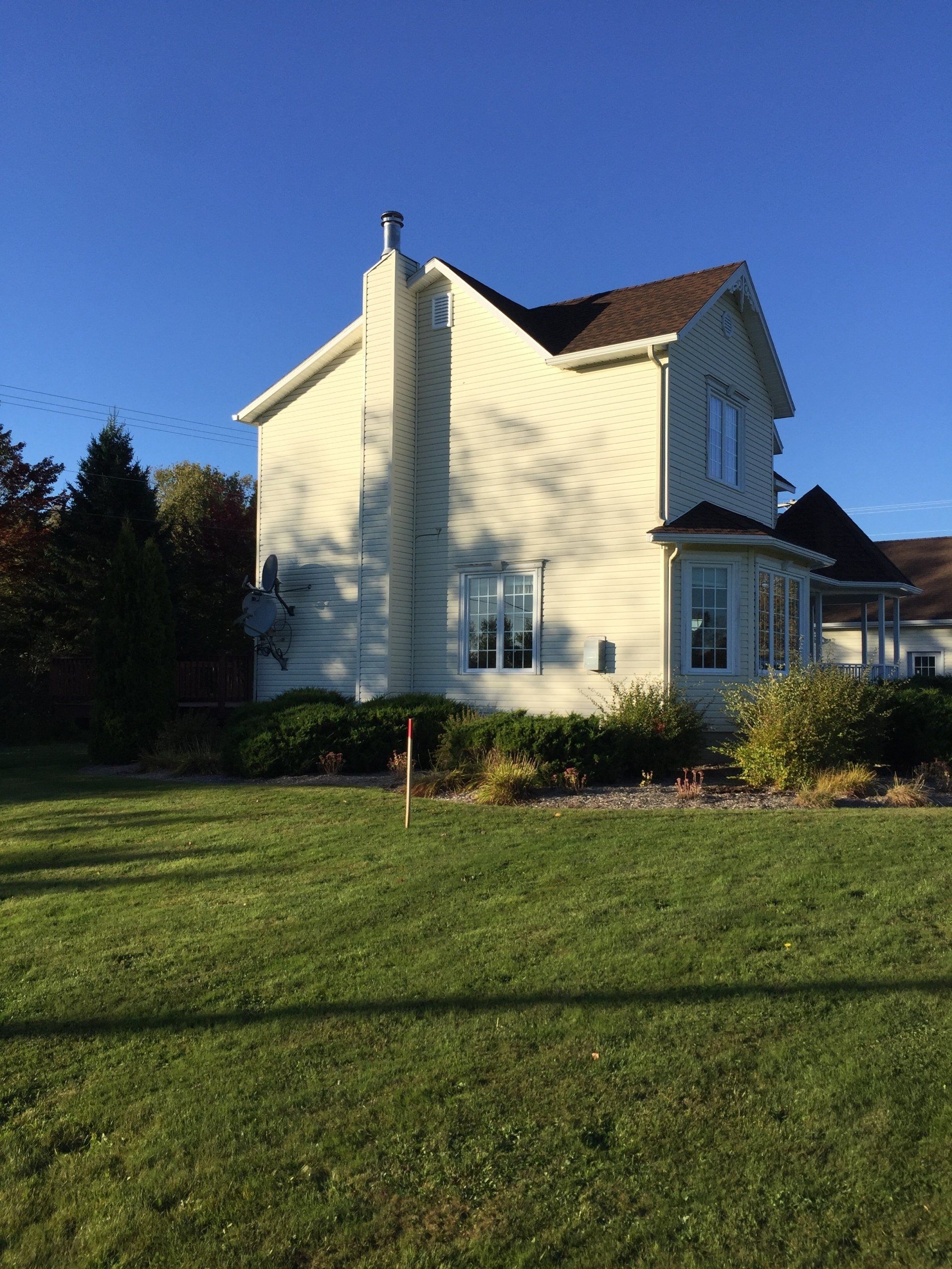 White two-story house with a red roof on a sunny lawn under a blue sky