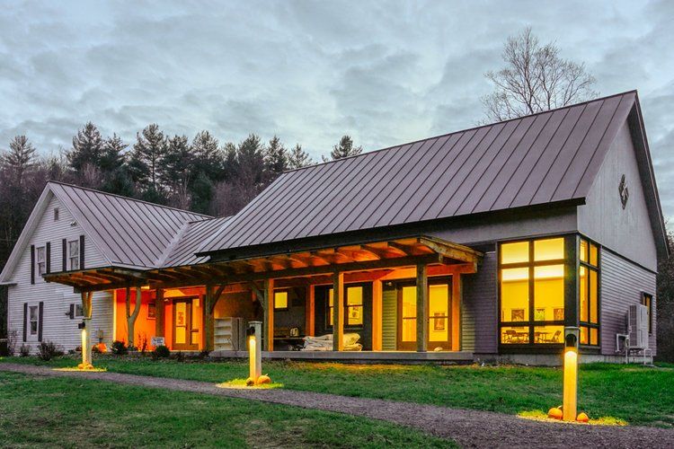 Modern barn-style building at dusk with warm-lit windows and a covered entrance in a grassy setting