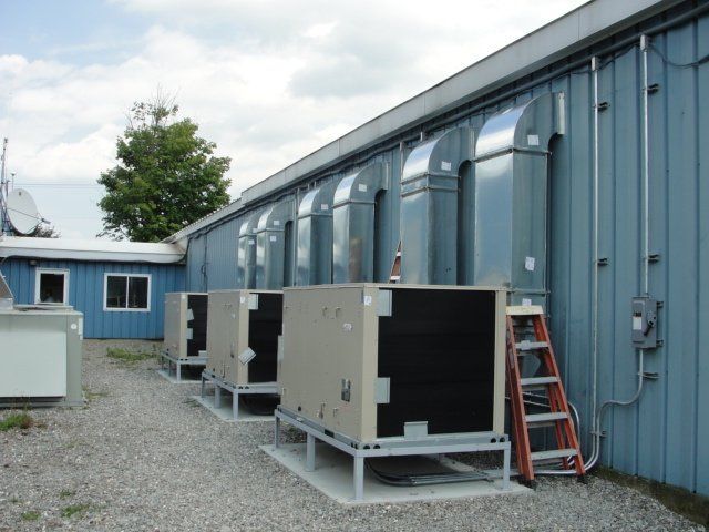 Outdoor industrial equipment units beside a blue metal building, with a red ladder leaning against the wall.