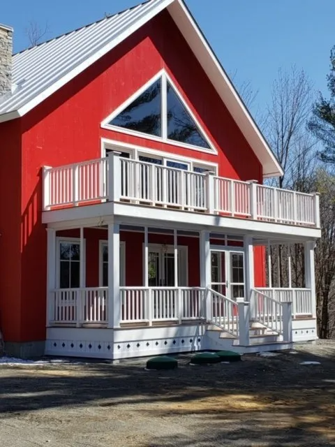 Red house with white trim, balconies, and large triangular windows in a snowy yard.