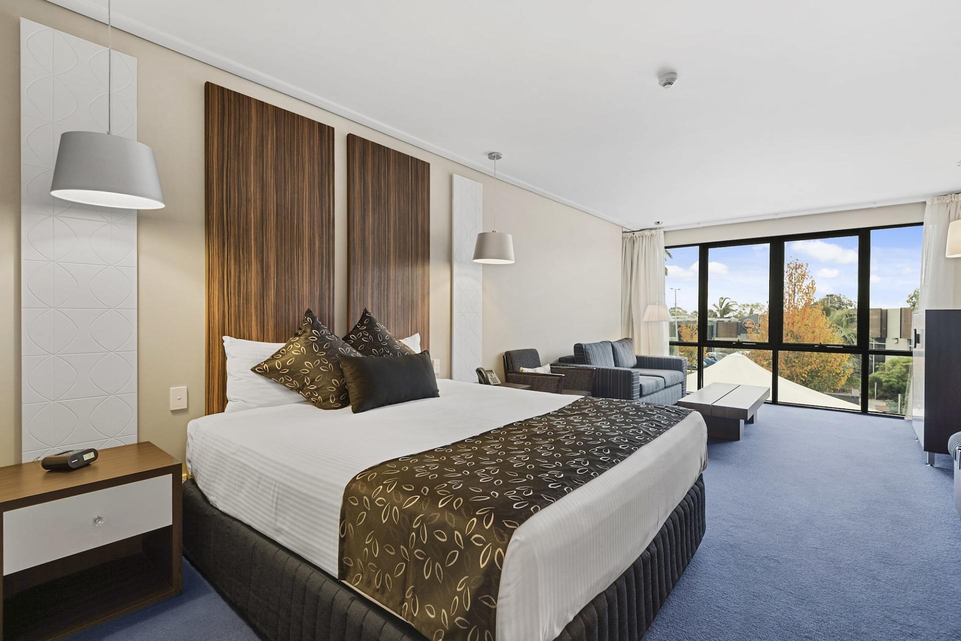 Hotel room with king bed, sofa, and large windows overlooking trees.