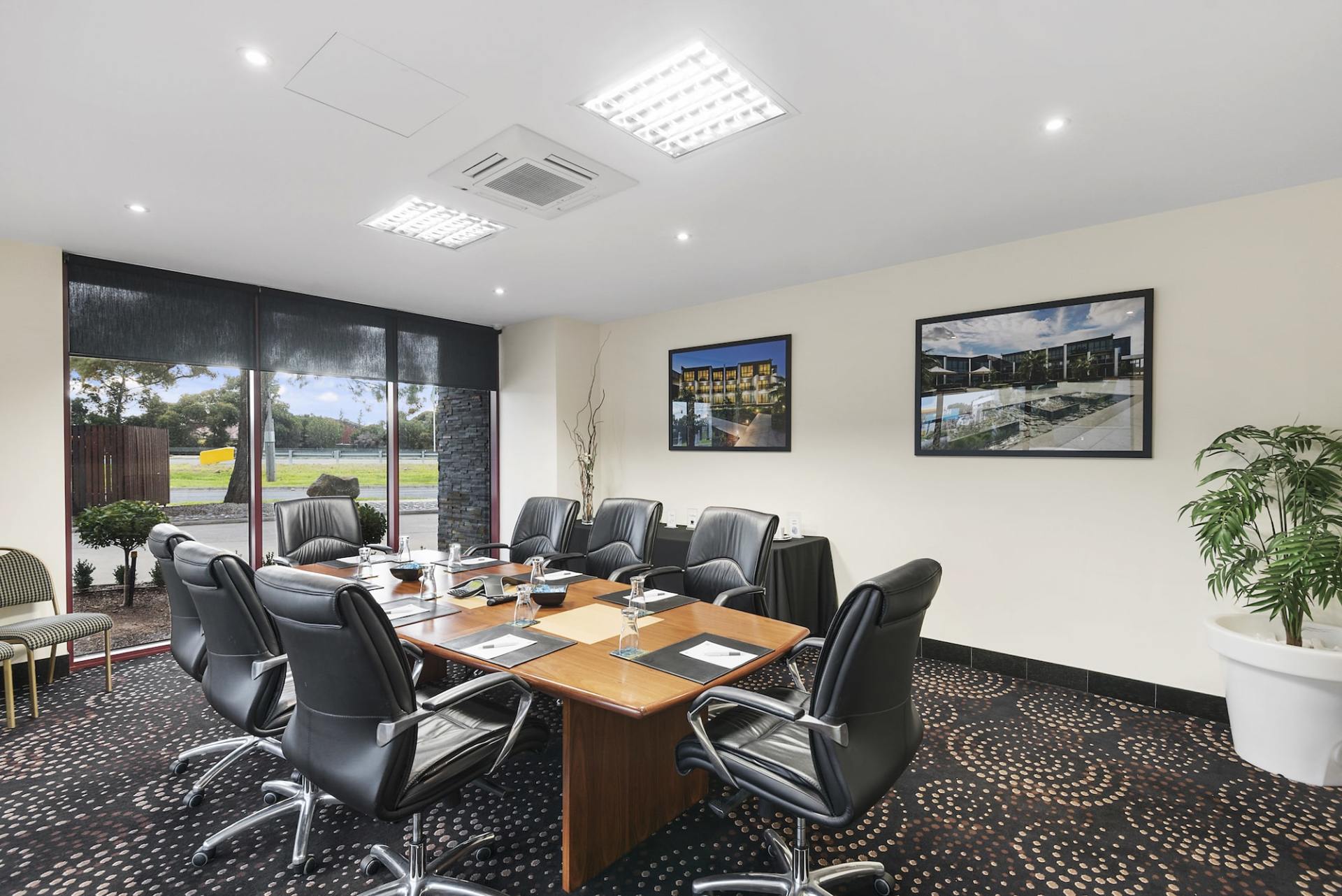 A boardroom with a large table, black chairs, and a window overlooking a grassy area.