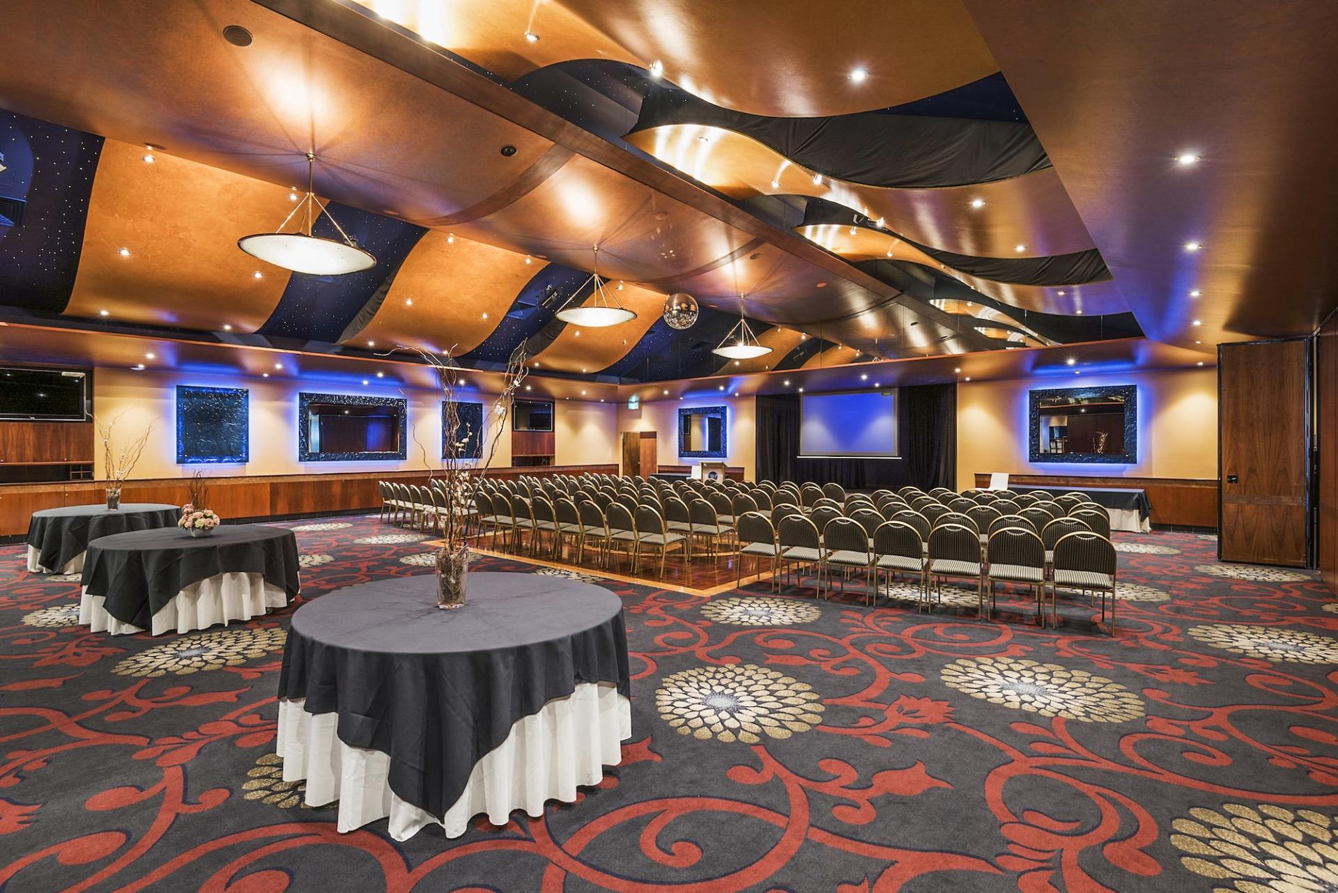 A large event space with round tables, rows of chairs, and a decorative ceiling and carpet.