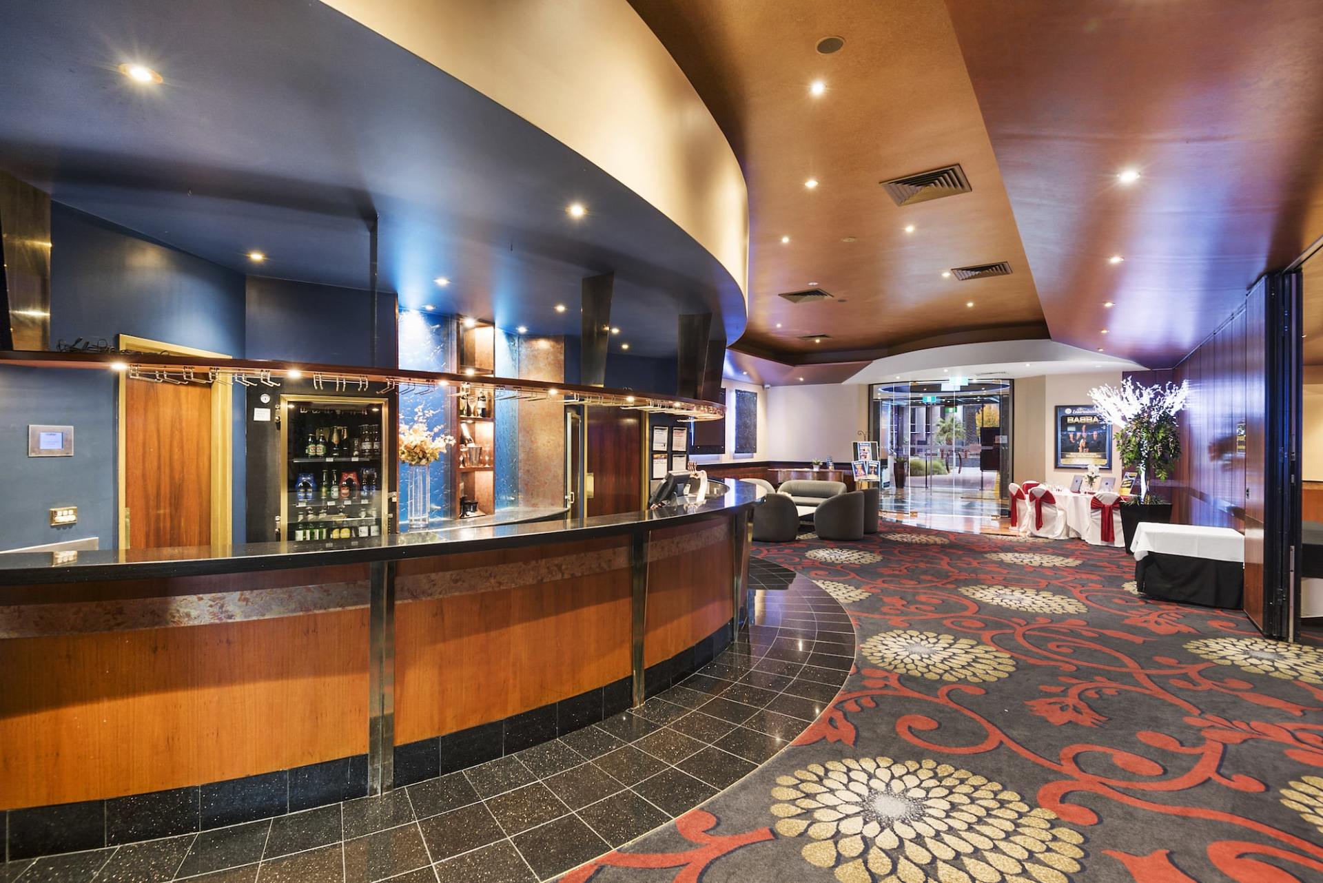 Interior view of a bar area with a curved wooden bar, patterned carpet, and seating in a hotel or event venue.