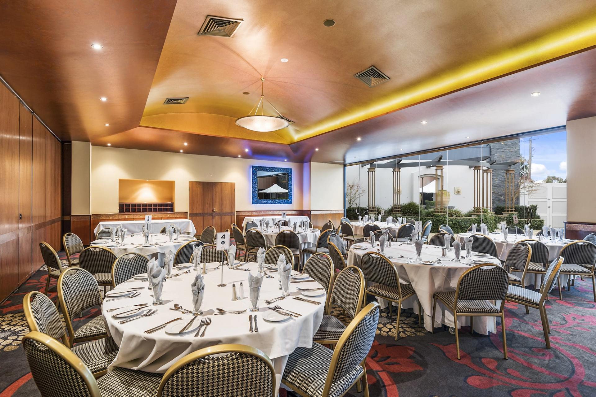 Banquet hall with round tables set for dining, patterned chairs, and a large window.