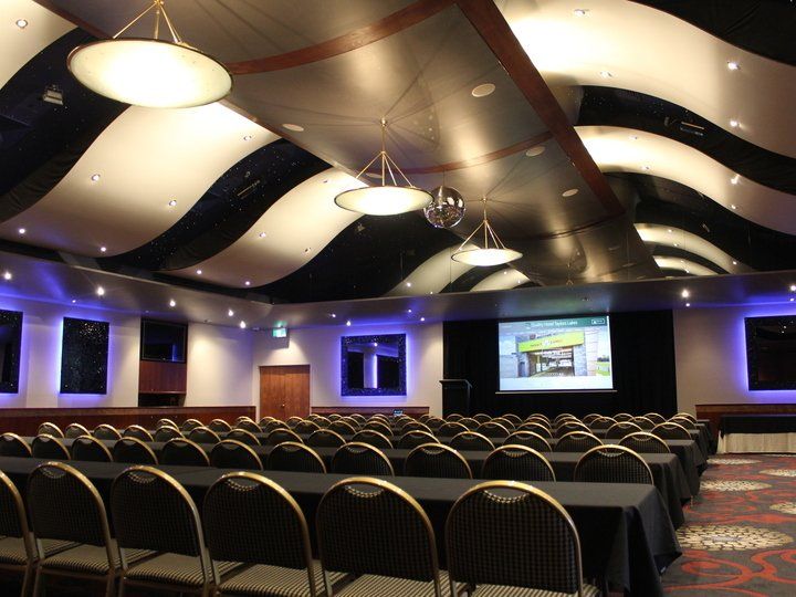 Auditorium with rows of chairs, a screen displaying an image, and an abstract black and white ceiling.