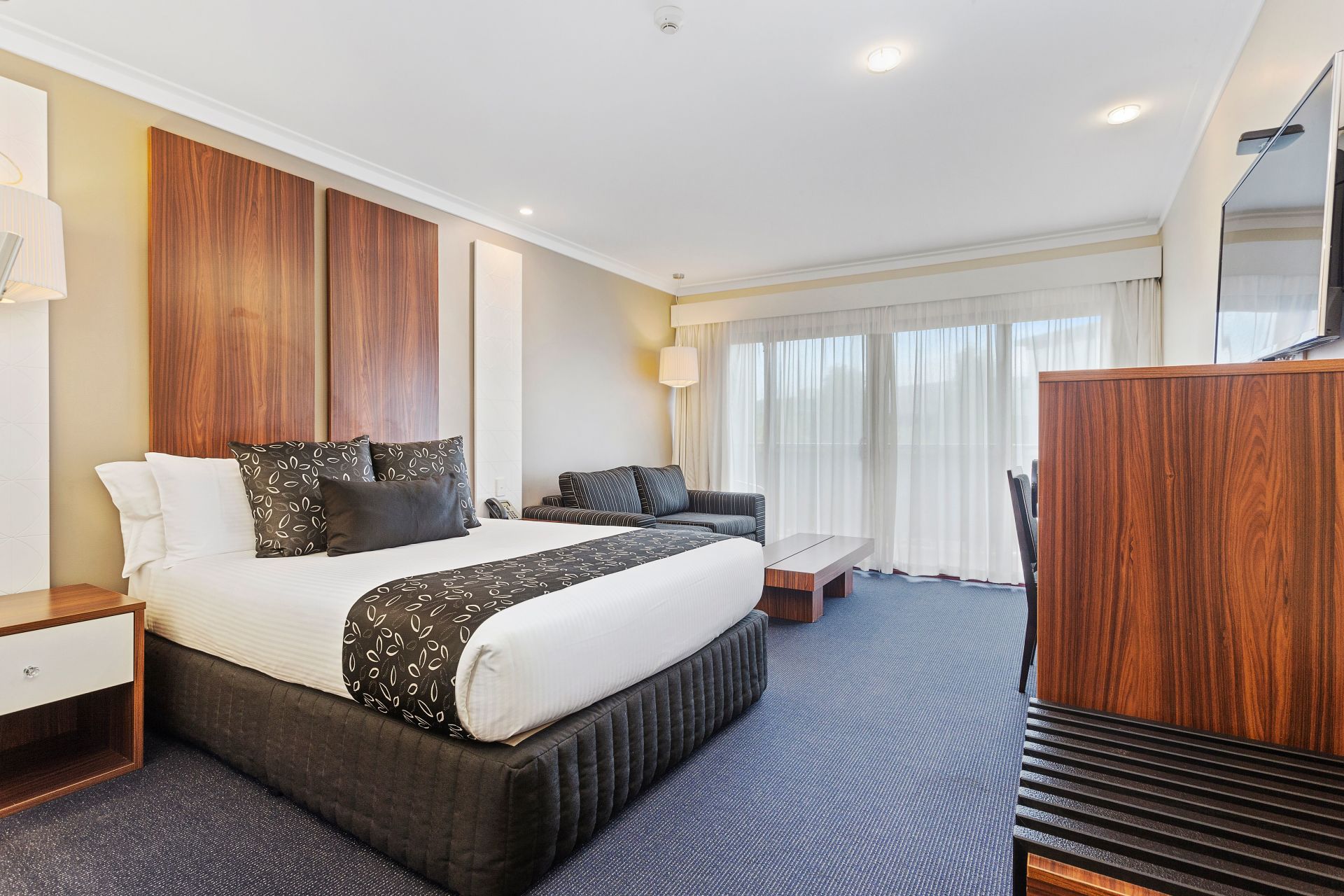 Hotel room with king bed, sofa, large window, wood accents, and blue carpet.