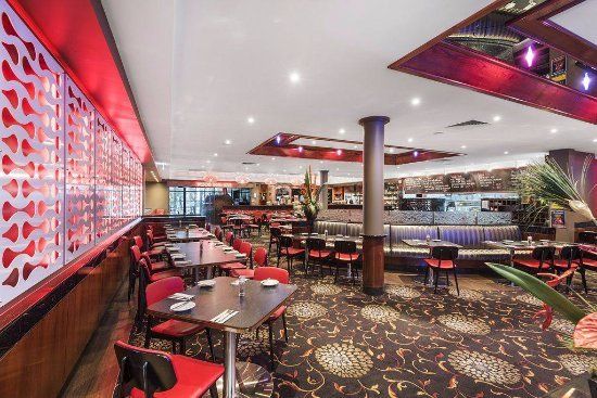 Restaurant interior with red accents, tables, and chairs; floral carpet.