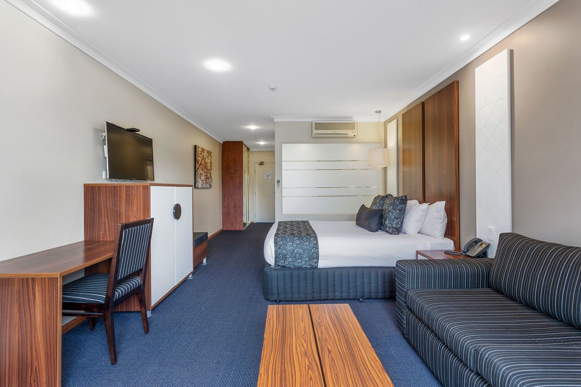 Hotel room with a bed, couch, desk, and TV on a blue carpet.