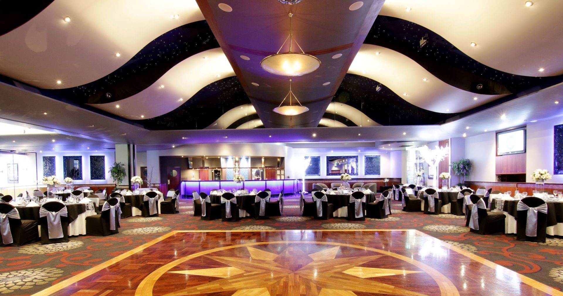 Ballroom with round tables, dance floor, patterned ceiling and black and white decor.