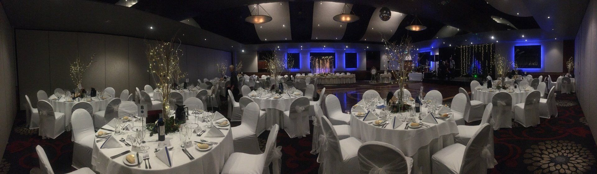 A banquet hall set up with round tables covered in white linens and chairs, and centerpieces ready for an event.