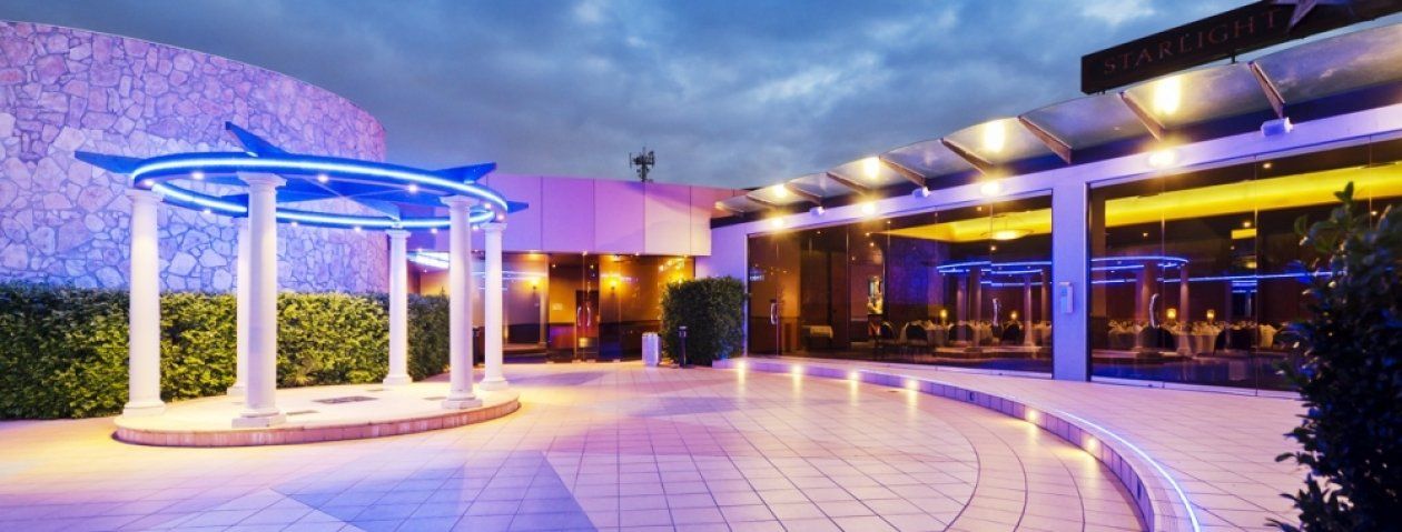 Exterior of a building with a blue-lit gazebo in front and the sky at dusk.
