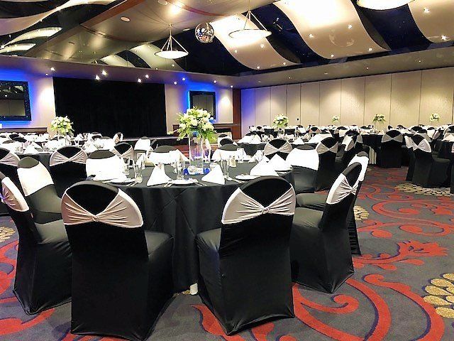 Banquet hall with black tablecloths, chairs with white bows, and floral centerpieces.