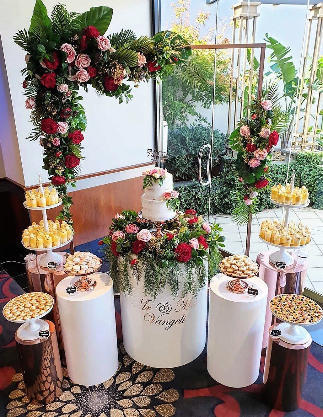 Wedding dessert table with cake, flowers, and treats on pedestals.