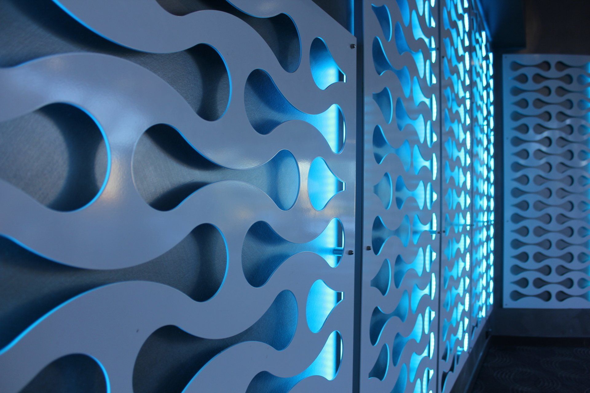 White, laser-cut wall panels with wave-like patterns, backlit by blue light, create a decorative architectural detail.