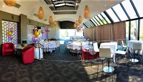 Event space: Tables set with white linens, red armchairs, balloon decorations, and hanging lights.