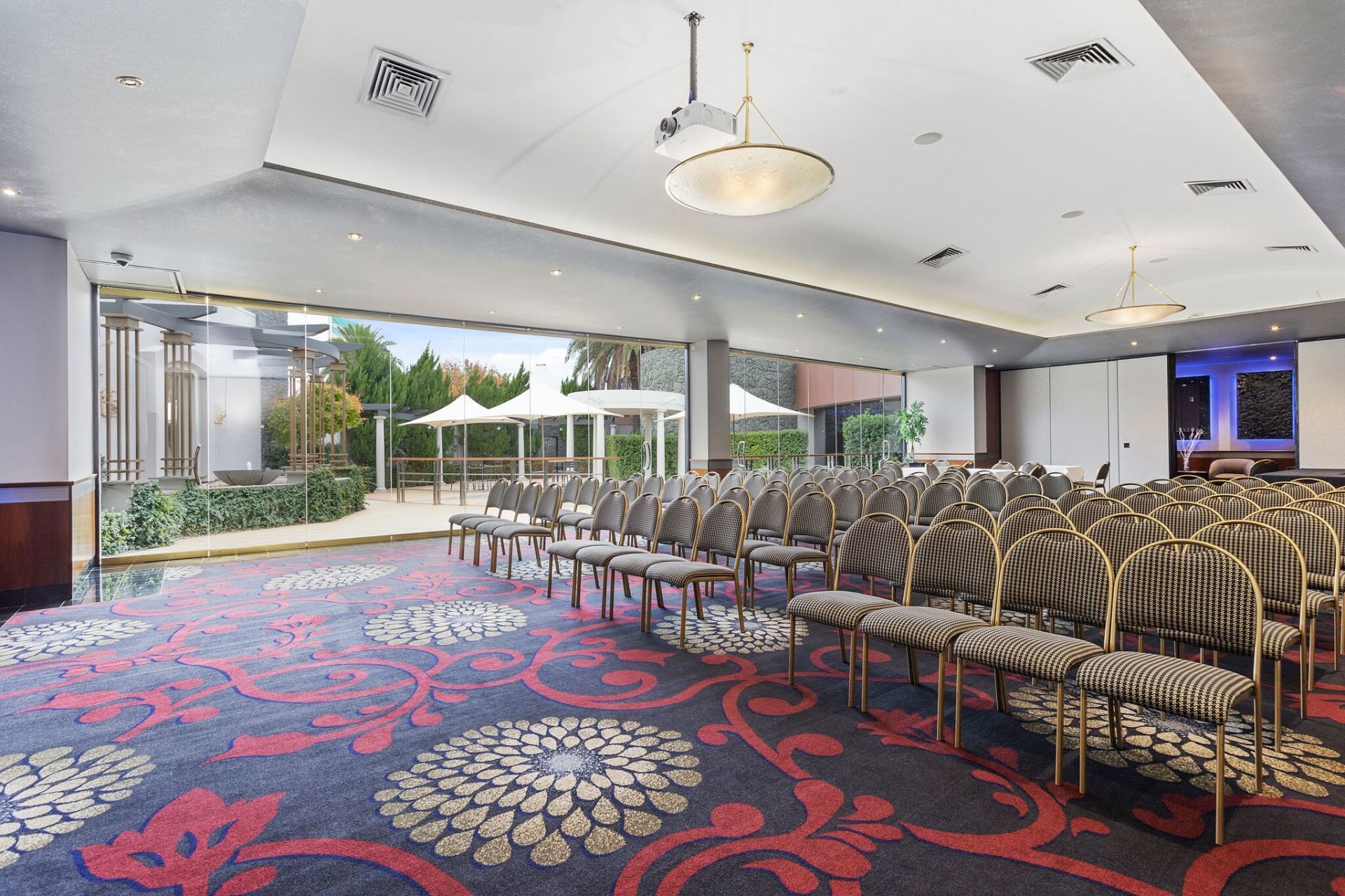 Conference room with rows of chairs, open doors to outdoor patio, floral carpet.