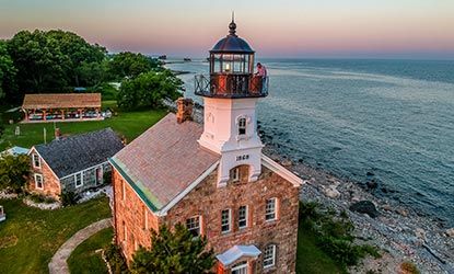 An aerial view of a lighthouse on a cliff overlooking the ocean.
