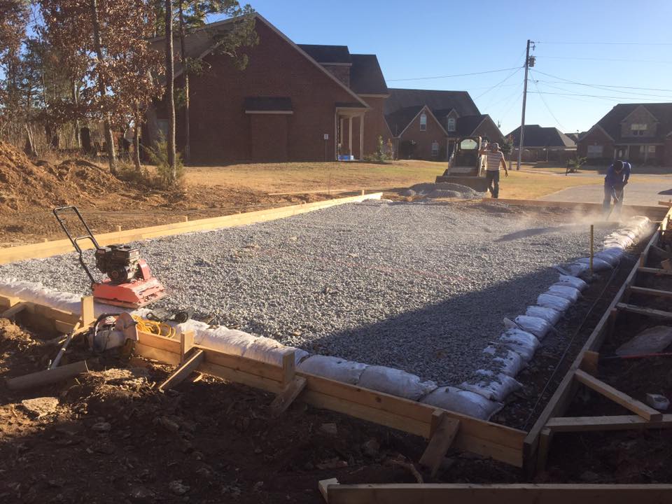 Road construction with fresh gravel, wooden forms, and workers paving a residential street.