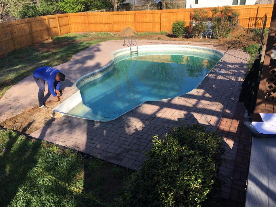 Person cleaning the edge of an outdoor swimming pool in a sunlit backyard