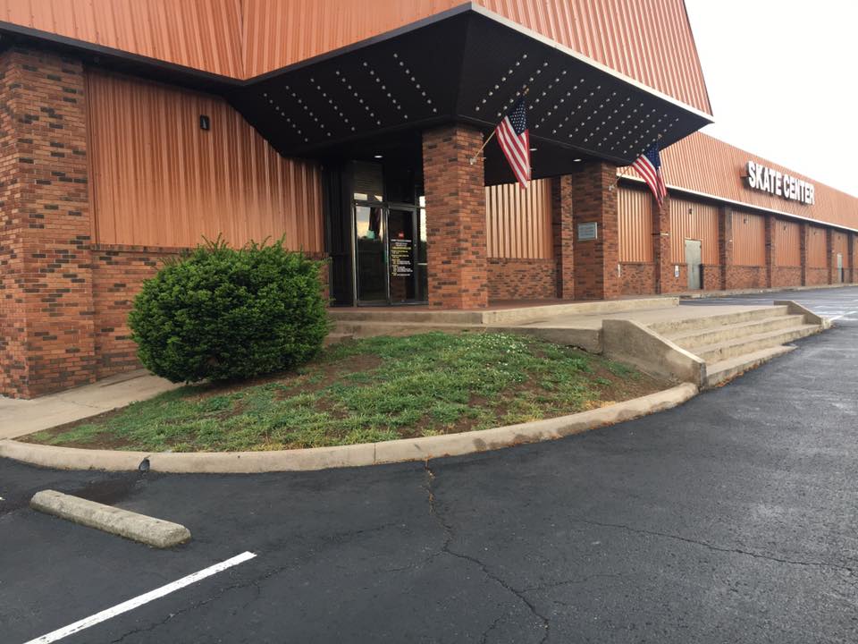 Brick storefront with orange awning, American flag, and wheelchair-accessible entrance ramp by parking lot