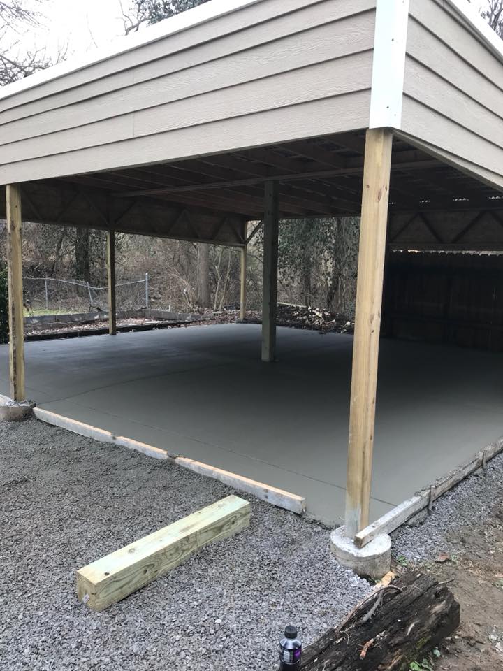 Partially built open-sided shed with concrete floor and wooden posts in a wooded area