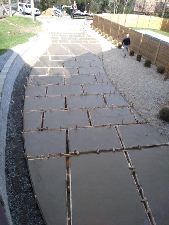 Steep paved walkway with uneven slab joints beside gravel, with a person walking a dog in the distance