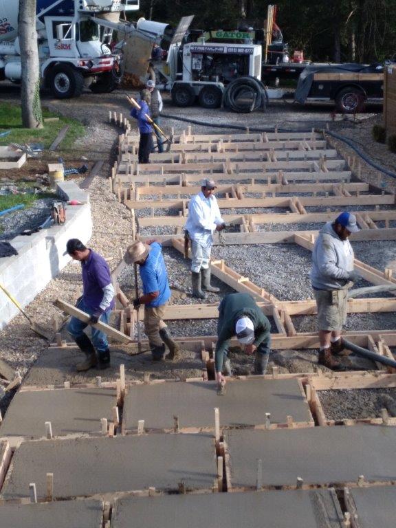 Workers paving a stepped concrete walkway on a hillside construction site with trucks above.