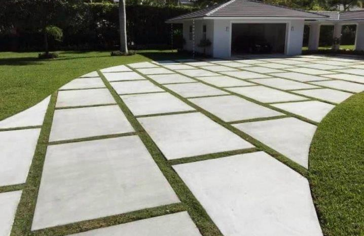 Concrete driveway with large square slabs and grass joints leading to a white house with an open garage