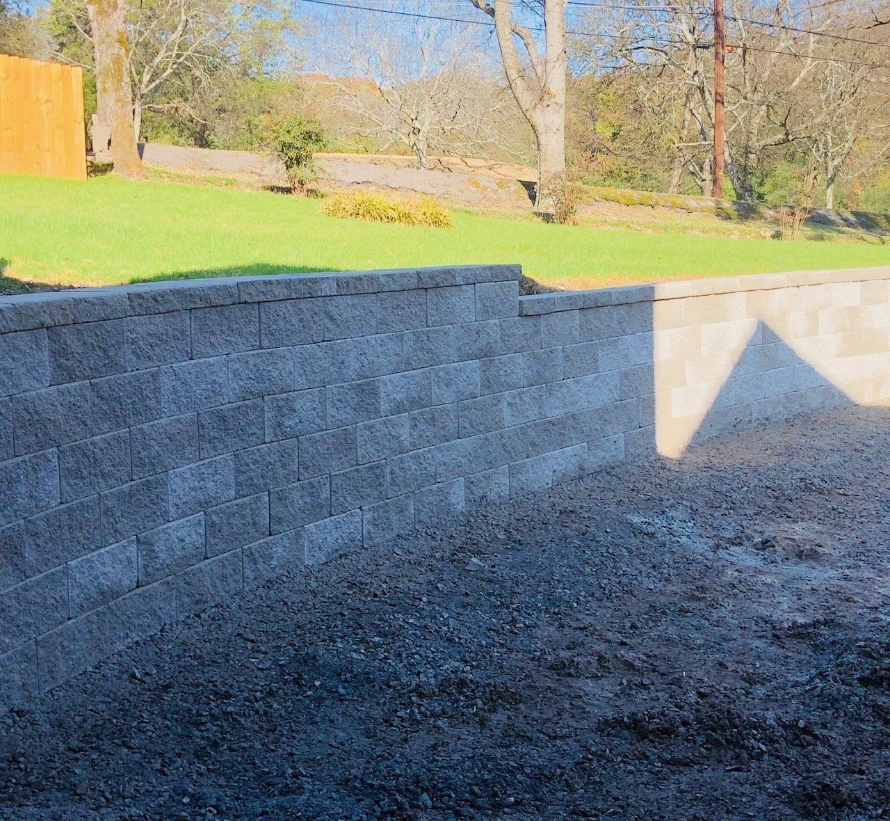 Stone retaining wall beside a gravel slope with grass and trees in bright sunlight