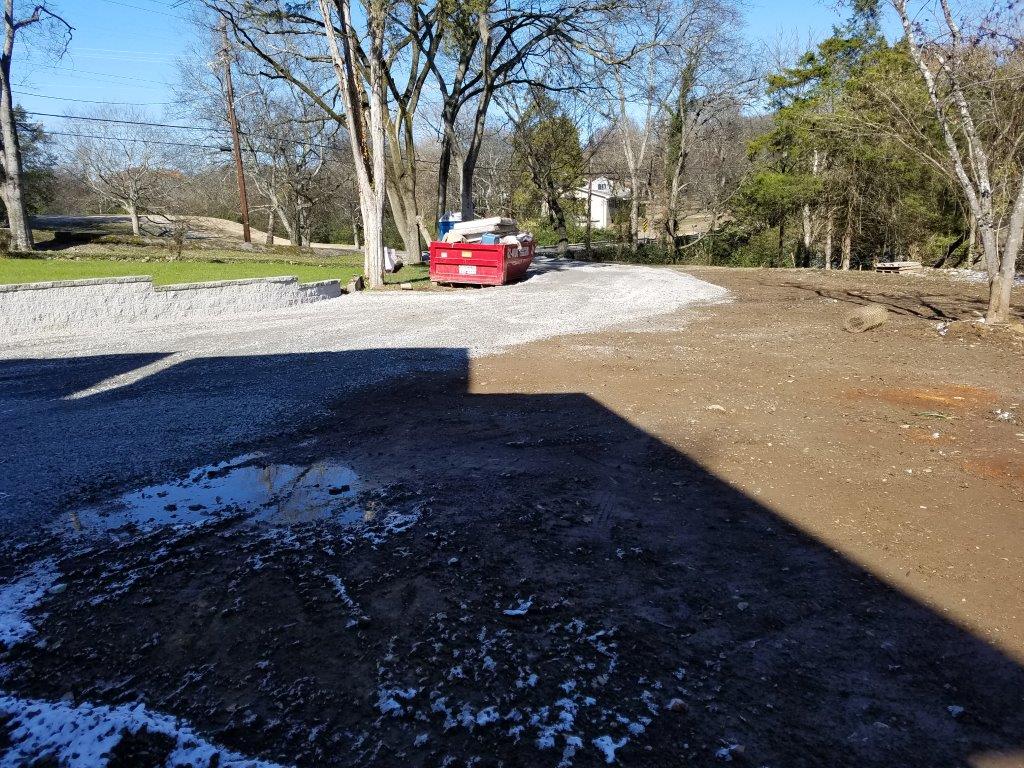 Red car parked on a gravel lot beside leafless trees in bright sunlight