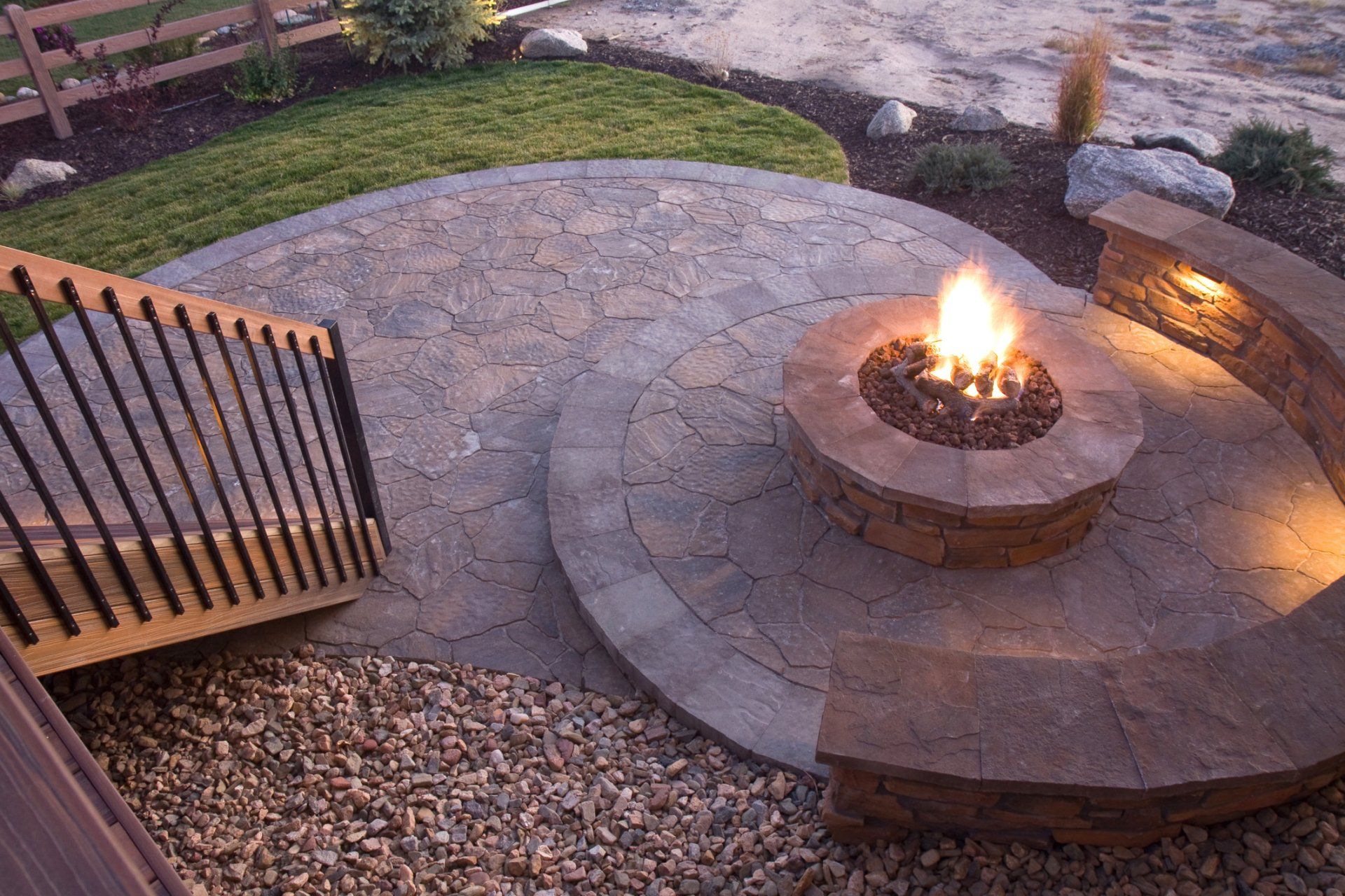 Circular stone patio with a central fire pit, surrounding seating wall, and a wooden gate at left