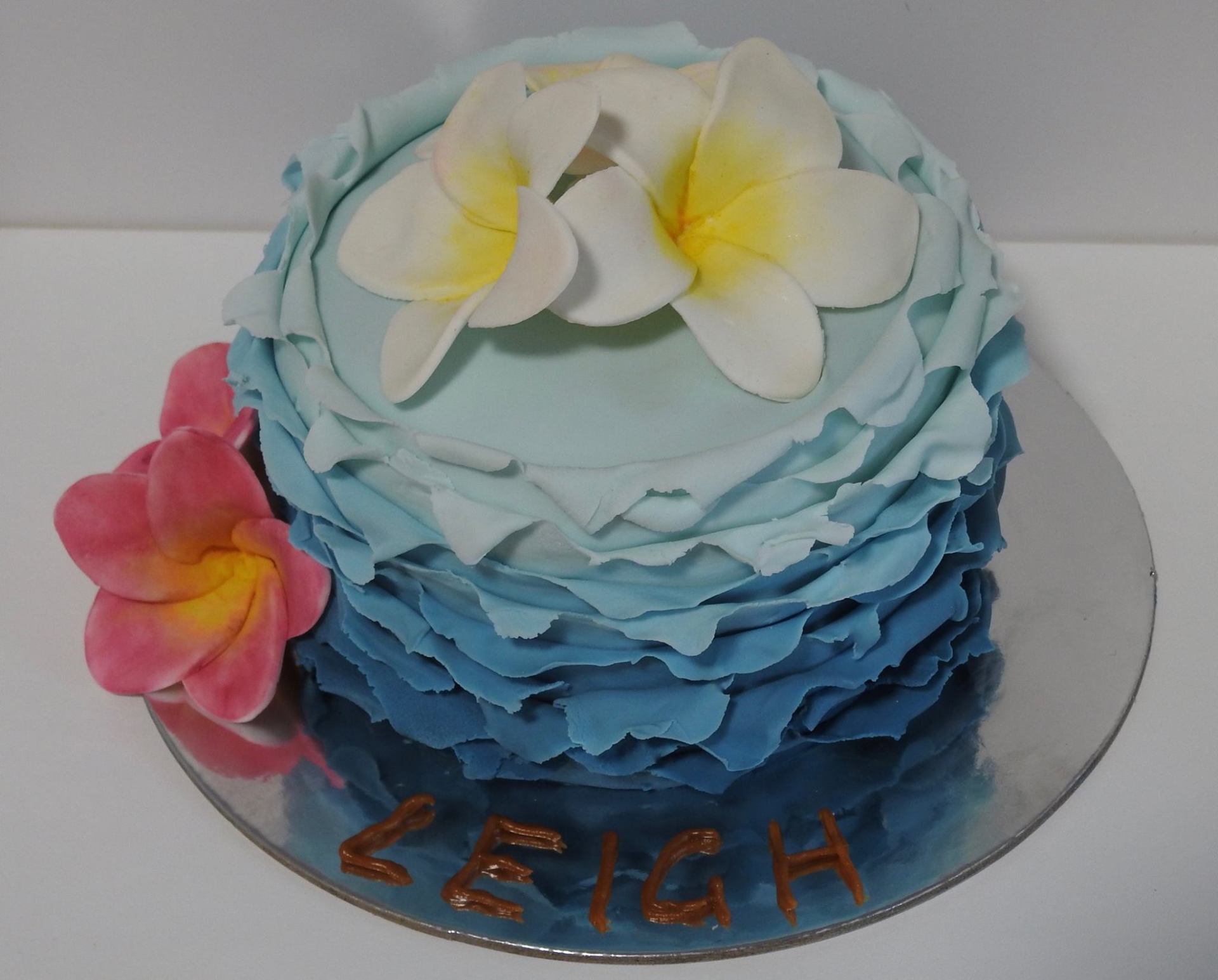 Small blue ombre ruffled birthday cake with hand made sugar Frangipanis in white and pink