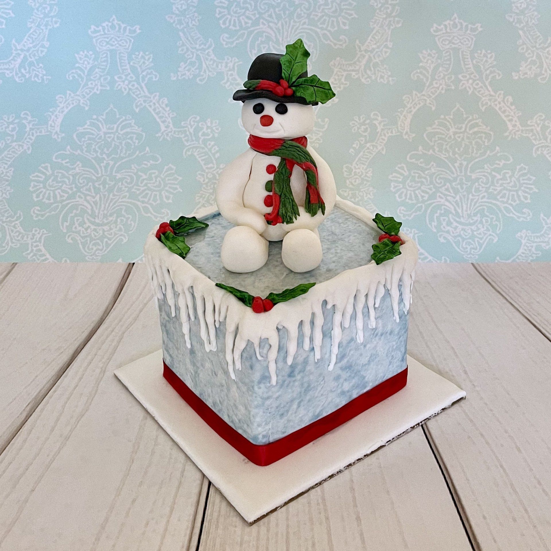 Christmas cake with hand sculpted fondant snowman, fondant icicles and fondant holly.