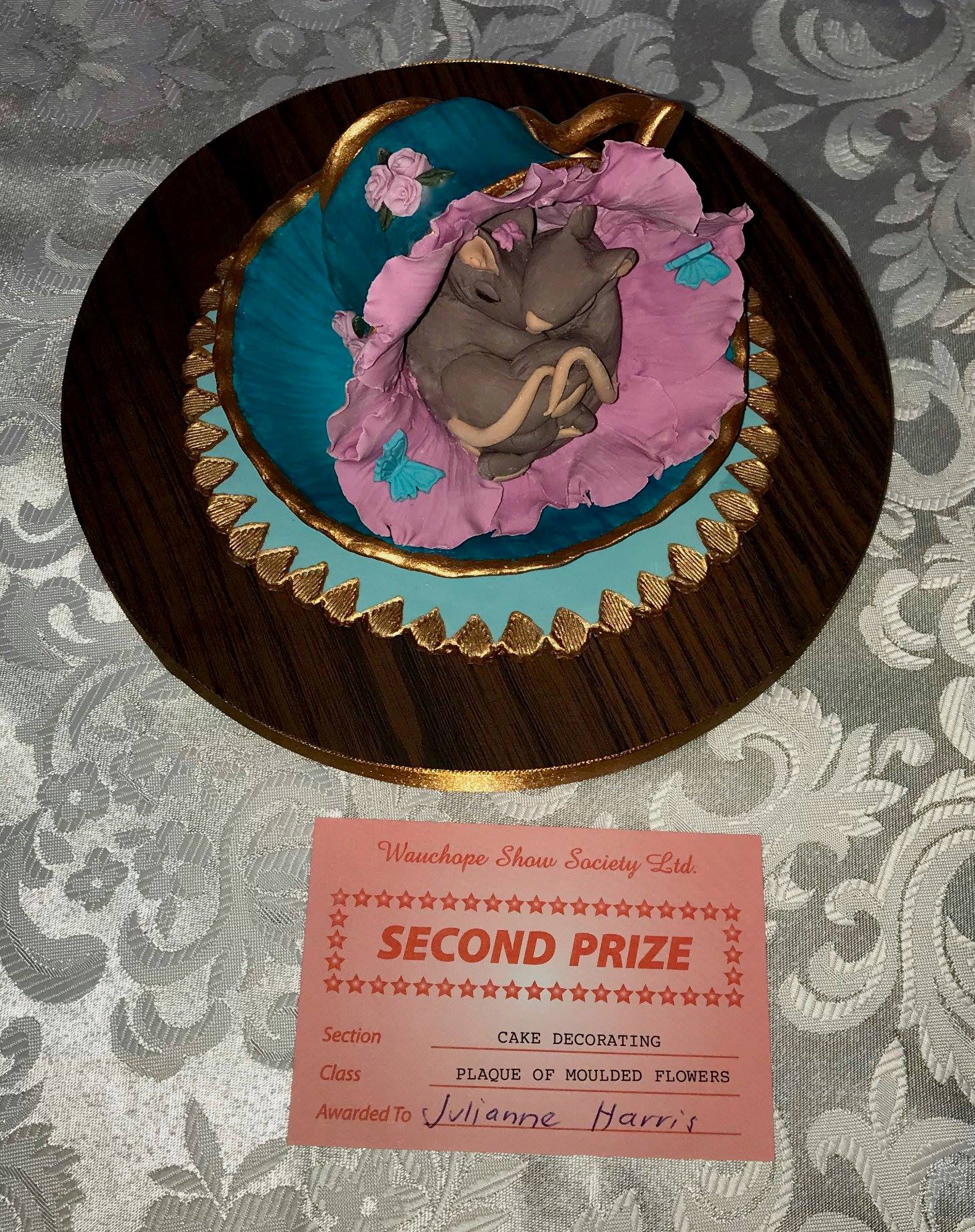 Cake topper of two very cute mice sleeping in a flower inside an ornate teacup.