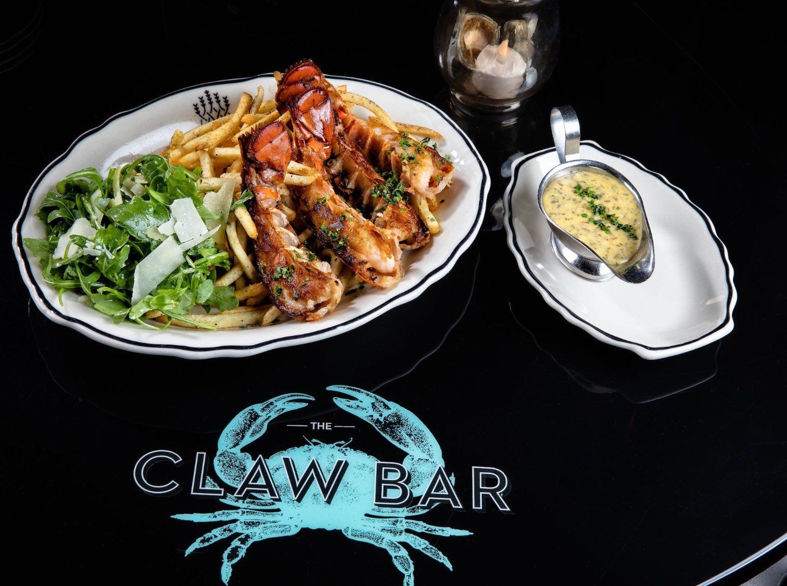 Plated seafood meal with greens and fries on a black Claw Bar table