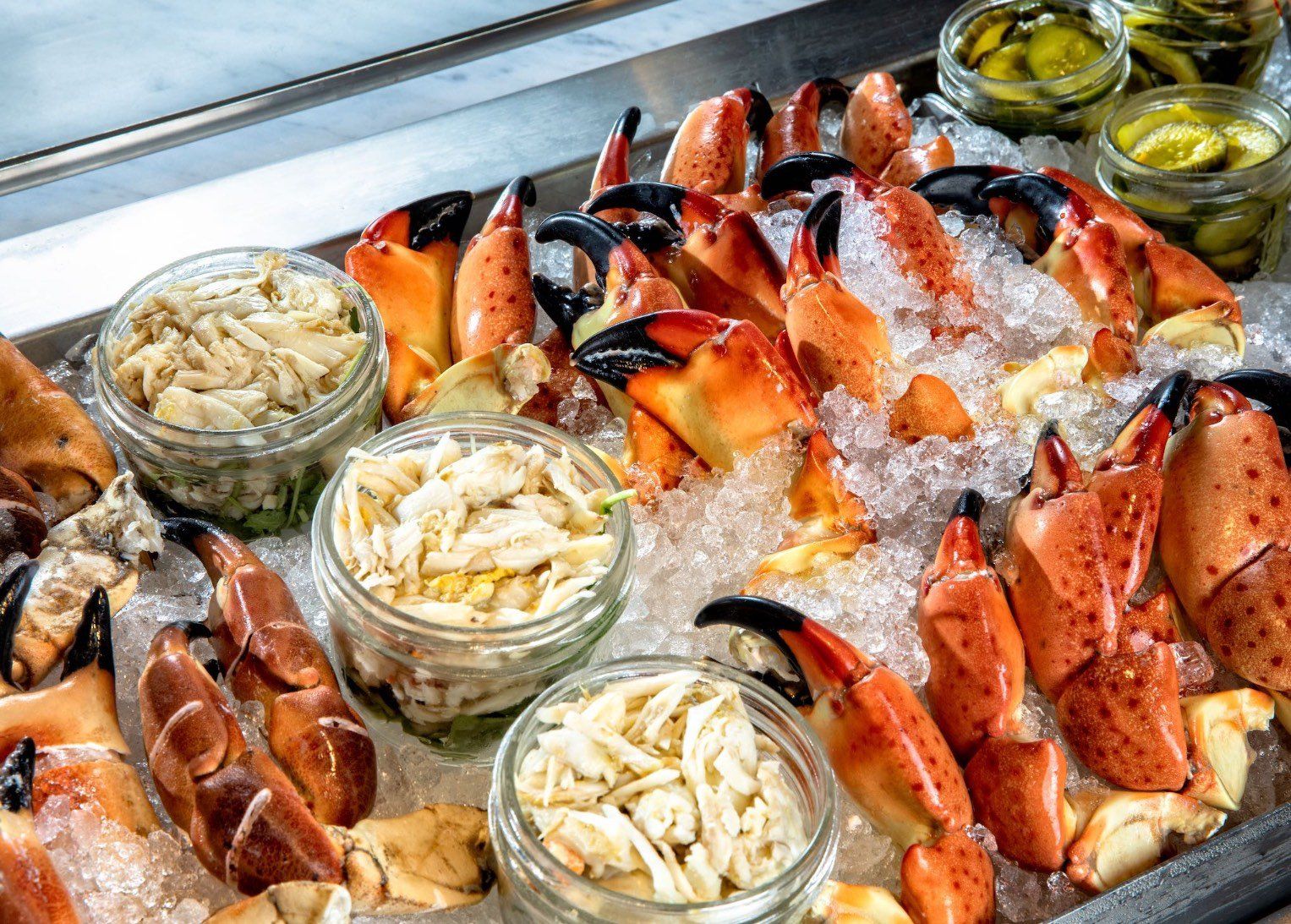 Tray of chilled crab legs and seafood on ice, with lemon wedges and small cups of sauce