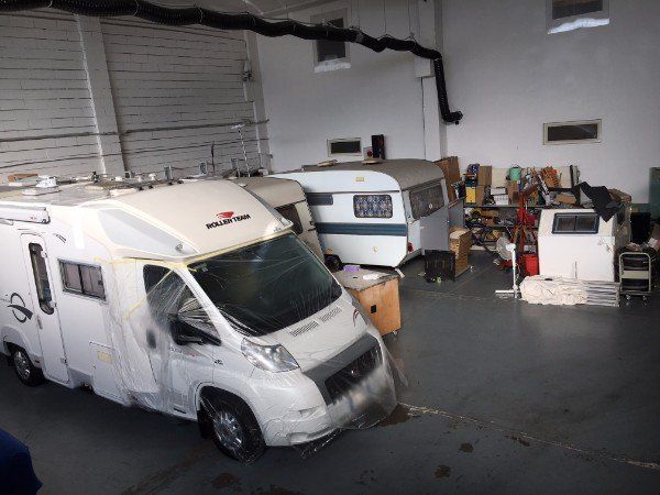Un camper in un garage con la parte anteriore danneggiata, accanto a un altro camper e ad attrezzature ammassate.