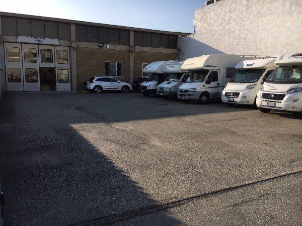 Area commerciale con furgoni bianchi parcheggiati accanto a un magazzino in mattoni in una giornata di sole.
