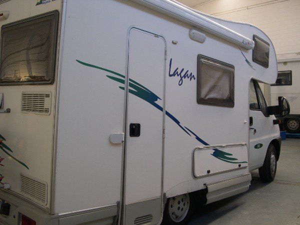 Un camper bianco con strisce grafiche blu e verdi è parcheggiato all'aperto.