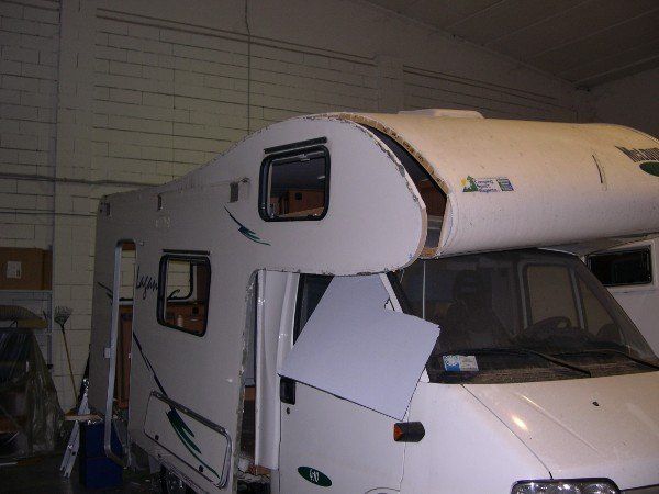 Camper bianco con gravi danni al tetto, parcheggiato in un garage o in un'officina.