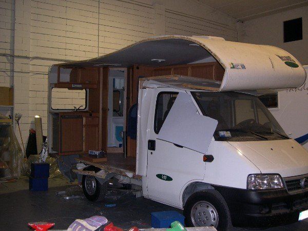 Un camper bianco con il tetto squarciato all'interno di un garage, che lascia intravedere l'interno.