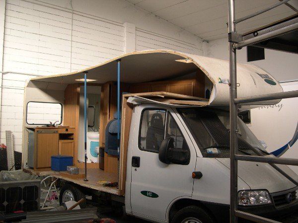 Un furgone bianco con interni in legno in stile camper, parcheggiato in un garage e visto di lato.