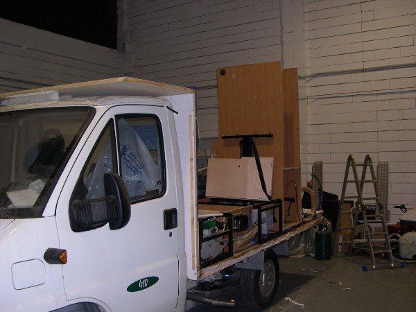 Un furgone bianco da lavoro in un garage, con il lato laterale aperto e attrezzi e armadietti visibili sul retro.