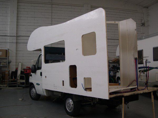 Camion bianco con un grande cassone camperizzato non rifinito all'interno di un'officina.