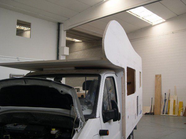 Un camper bianco parcheggiato all'interno di un garage/officina con il cofano aperto.